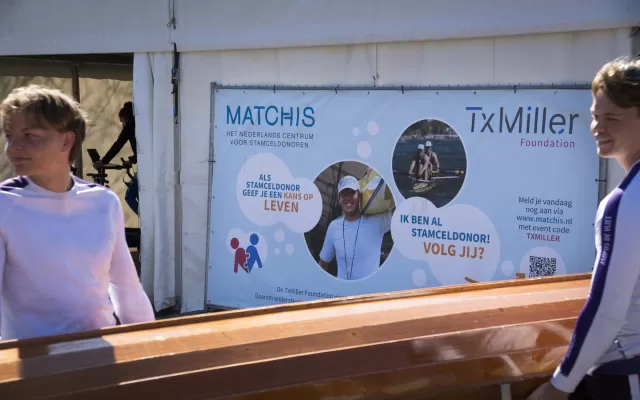 Twee jongen dragen een kano met een doek op de achtergrond waar het logo van zowel Matchis als TxMiller op te zien is